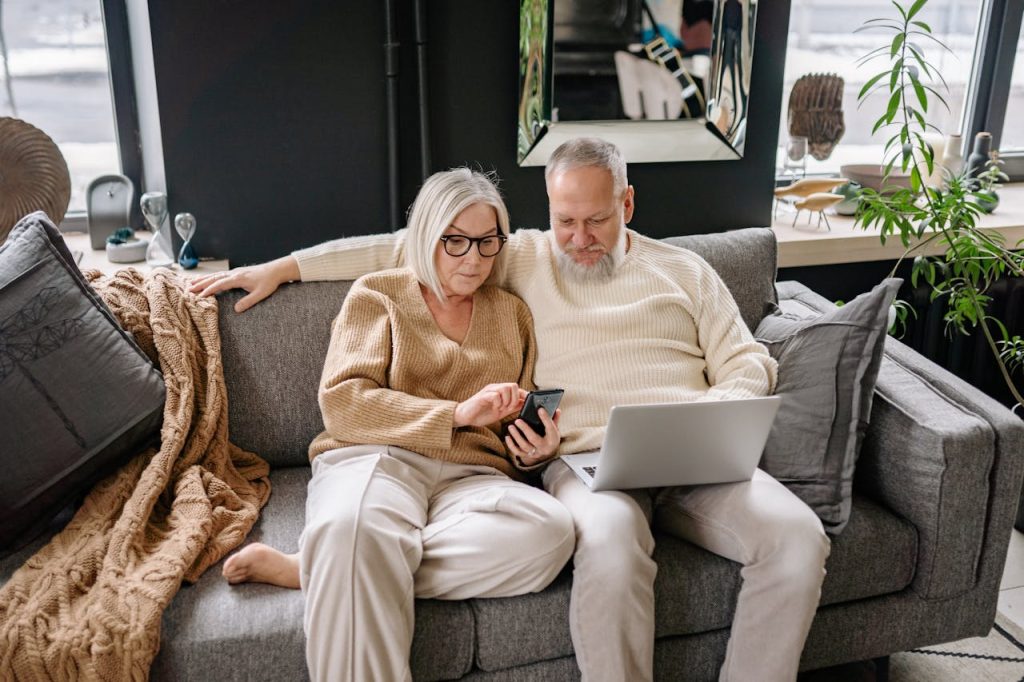 Older couple sitting together on a sofa using a smartphone and laptop
